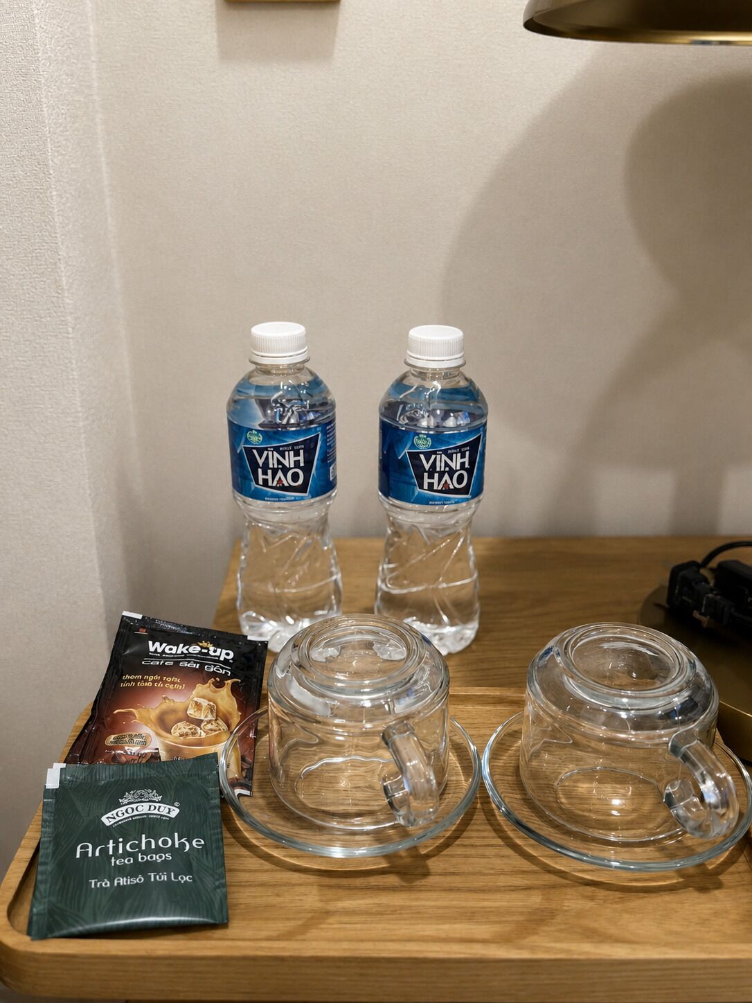 Two bottles of Vinh Hao water, two glass mugs, and a tray with a Wake-up tea bag and a packet of Artichoke tea bags.