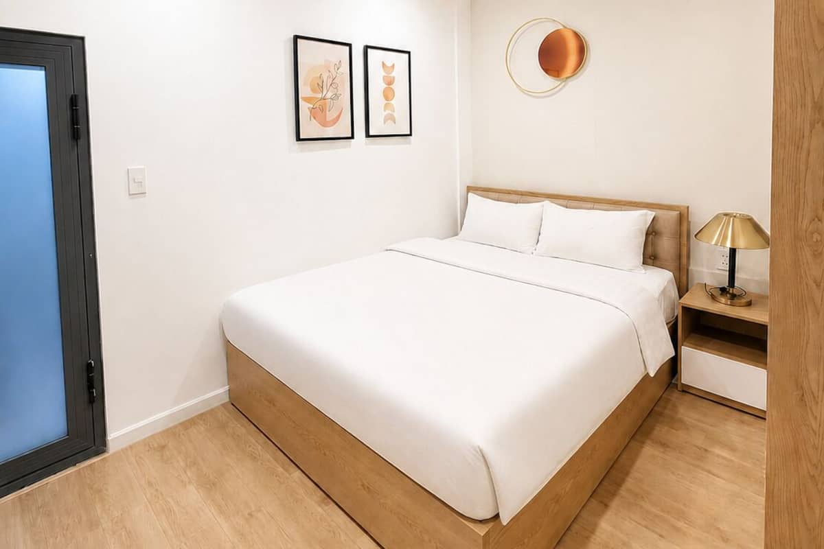 A bedroom with a bed, a nightstand, a wall-mounted light, and two framed pictures.