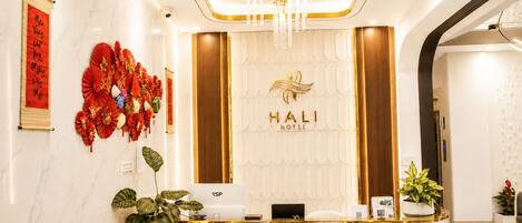 A hotel reception desk with a marble counter, a chandelier, and a wall with a logo and decorations.