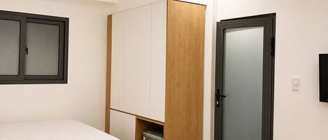 A hotel room with two beds, a wardrobe, a trash bin, and a television on the wall.