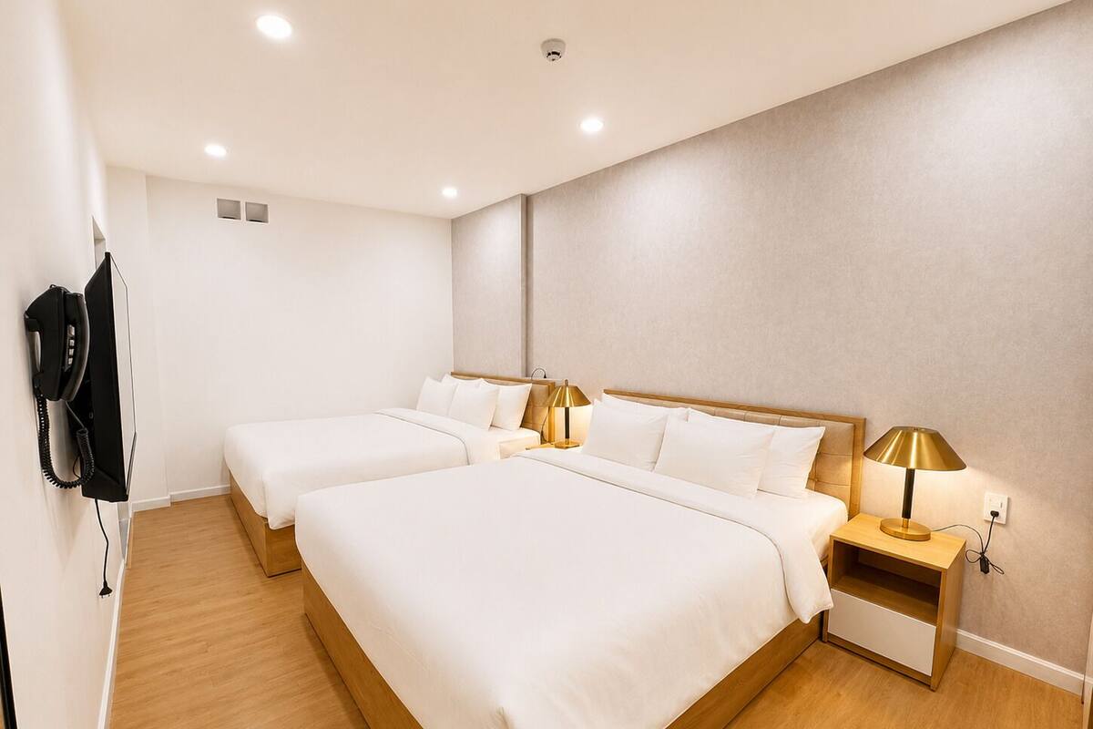 A hotel room with two beds, a bedside table with a lamp, a phone, and a wall-mounted light fixture.