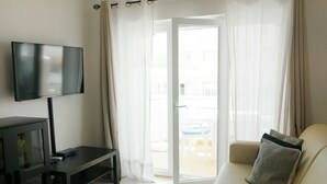 En stue med et fladskærms-tv, en sofa, et sofabord og en skydedør til et udendørs område.