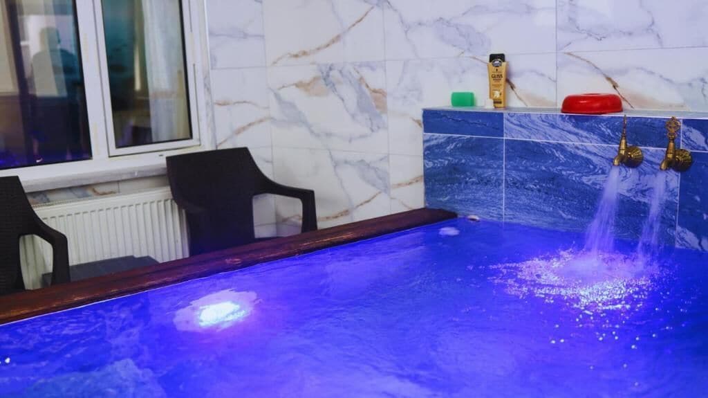 Una piscina con superficie iluminada en azul, una ventana con vistas y una pared de azulejos con diseño de mármol.