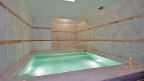 Ett spa-rum med ett rektangulärt bubbelbad, väggar i marmor och ett takfönster.