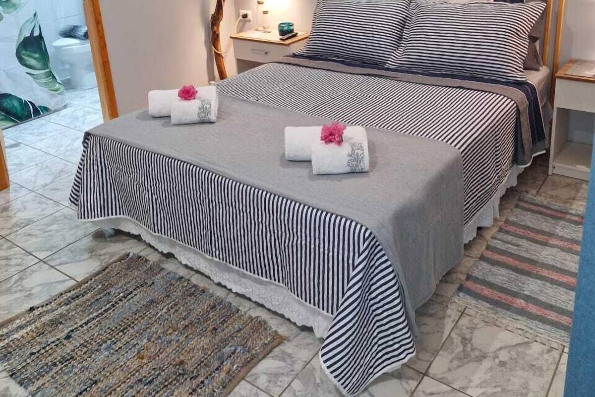 A bedroom with a bed, a nightstand, a wall-mounted artwork, a mirror, and a door leading to another room.