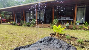 Une fontaine en pierre dans un jardin agrémenté d’une terrasse en bois et de plantes en pot.