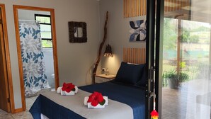 Une chambre à coucher avec un lit, une table de chevet, un miroir, une fenêtre avec des rideaux et une vue sur l’extérieur.