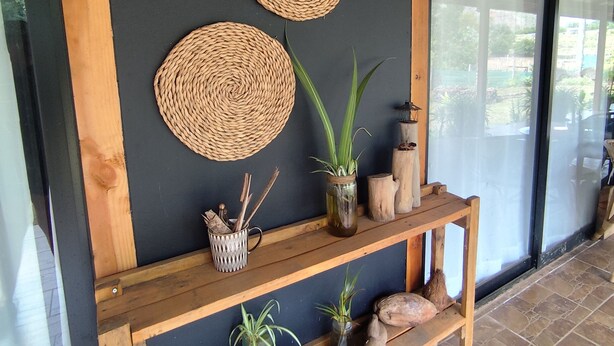 Un mur orné de paniers tressés, une étagère avec des plantes et des objets décoratifs, et un banc en bois.