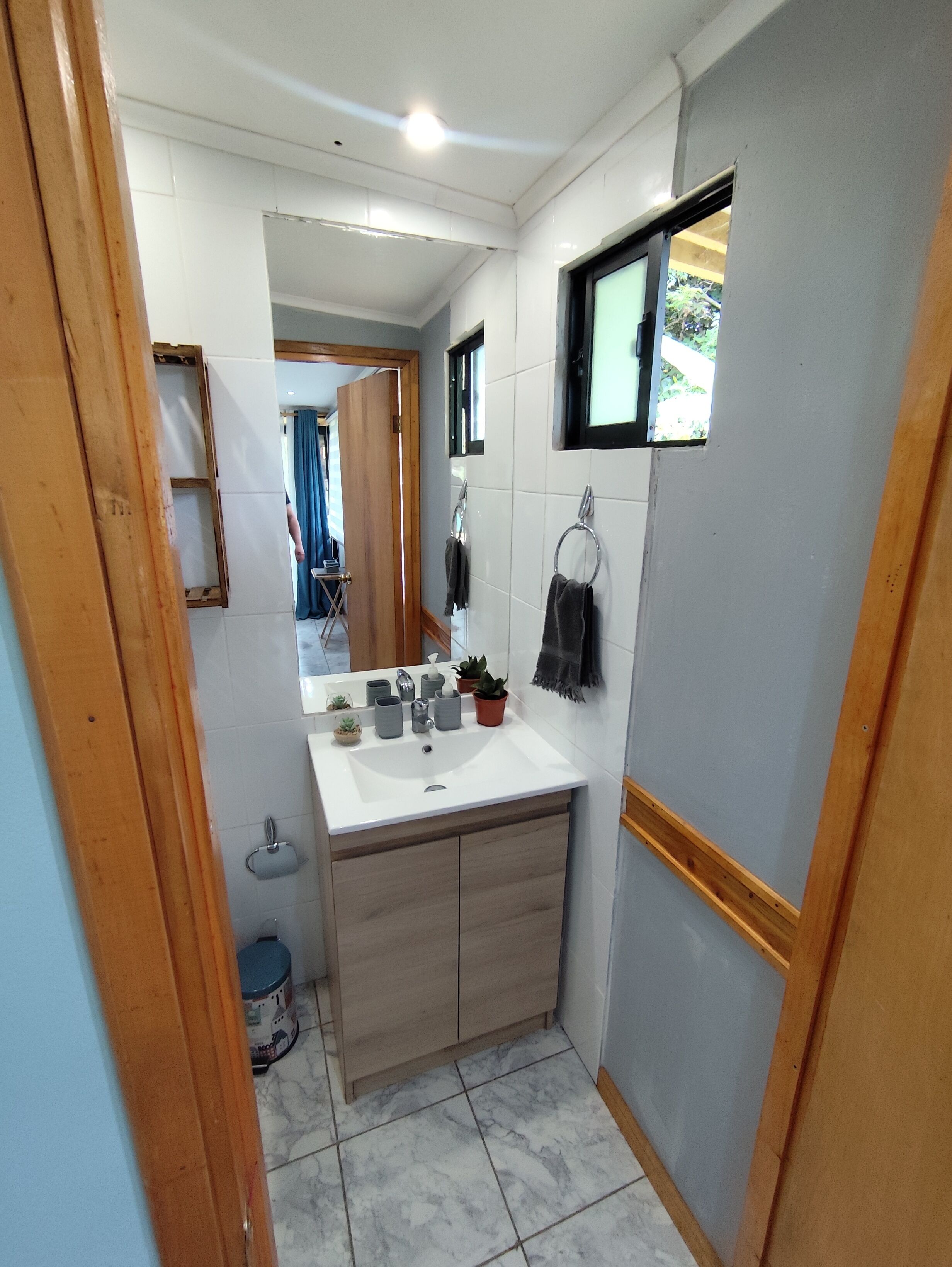 Un baño pequeño con un lavamanos blanco, armarios de madera y un ventanal.