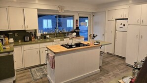 Una cocina moderna con armarios blancos, una isla central con estufa y vistas al mar a través de grandes ventanales.
