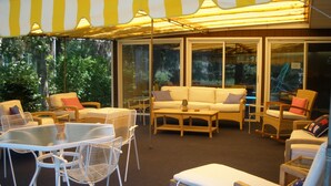 Un patio soleado con mobiliario de mimbre, un sofá blanco y una silla de descanso.