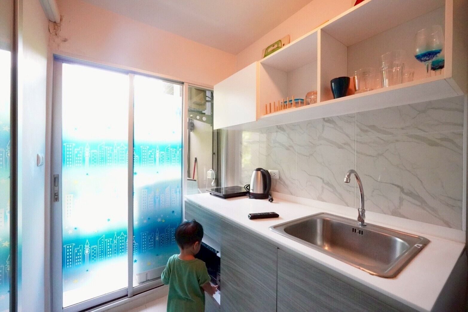 A modern kitchen with a large window, a stainless steel sink, and a kettle on the counter.