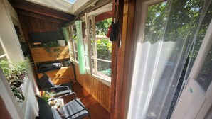 Ett soligt rum med trägolv, en svart stol, ett litet bord och en skjutdörr i glas som leder ut.