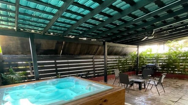 Een hottub onder een groen dak, omringd door stenen vloeren en tuinmeubilair.