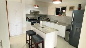 Een moderne keuken met witte kastjes, een centraal eiland met krukken, een roestvrijstalen koelkast en hanglampen.