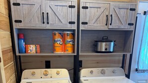 Two Maytag front-loading washing machines in a compact laundry room with wooden cabinetry and shelves holding cleaning supplies.