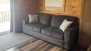 A cozy room with a grey sofa, wooden flooring, and a window with blinds.
