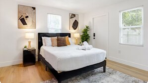 Ein modernes Schlafzimmer mit schwarzem Bettgestell, weißer Bettwäsche und zwei Nachttischlampen. Es sind abstrakte Wandbilder und ein Topfpflanze zu sehen.