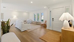 A spacious living room with a large sofa, a coffee table, and a chair. There is a door with a mirror and a lamp on a side table. - Luxury Coastal Retreat | Salt Water Heated Pool (Sanibel)