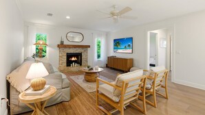 A living room with a fireplace, a ceiling fan, a sofa, a coffee table, and a TV. - Luxury Coastal Retreat | Salt Water Heated Pool (Sanibel)