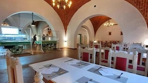 Ein Restaurant mit Ziegeldecke und gewölbten Nischen, weißen Tischen mit Speisekarten und roten Sitzgelegenheiten.