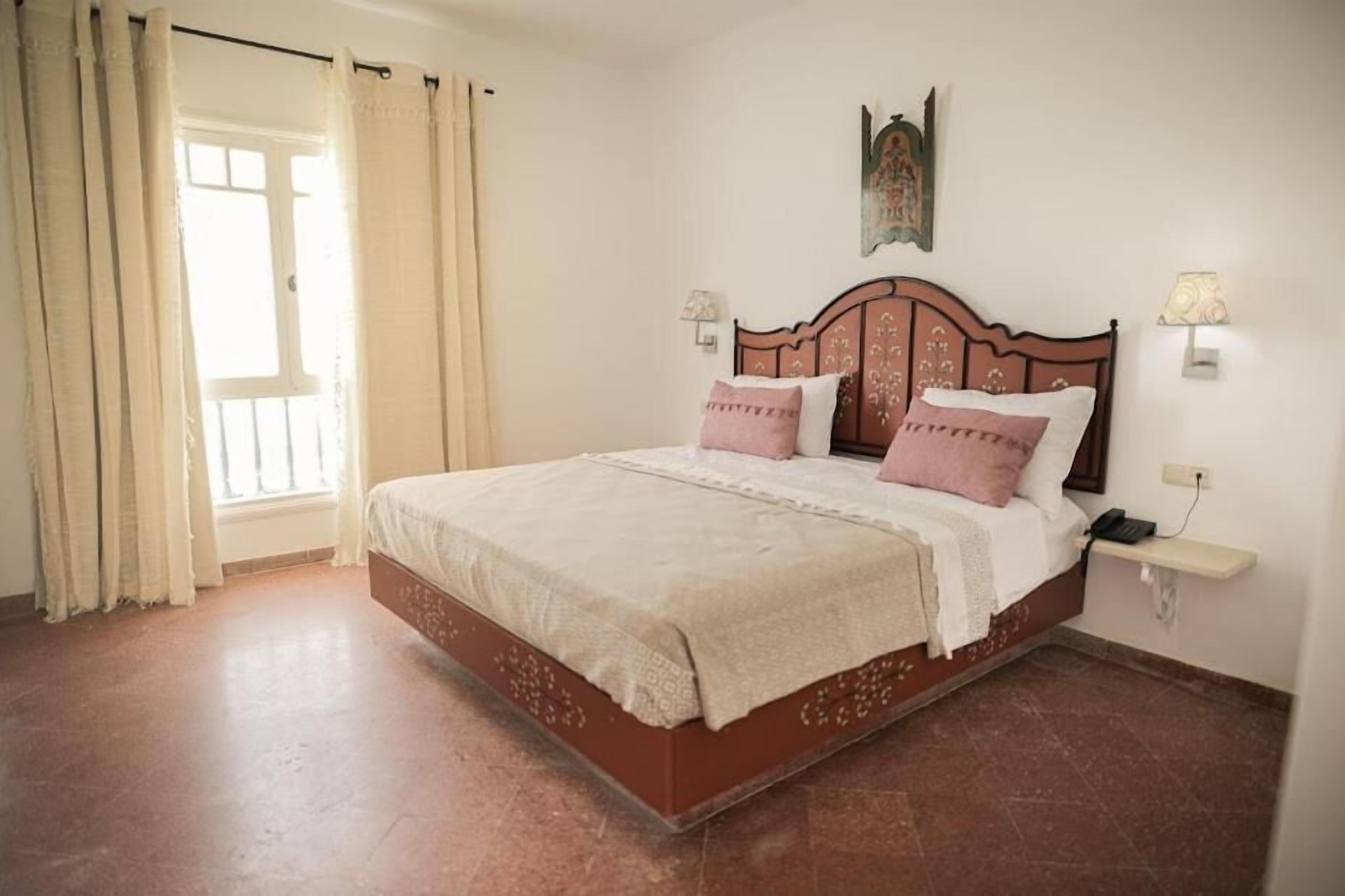 A bedroom with a bed, curtains, a nightstand, and a wall-mounted lamp.