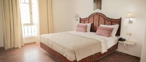 A bedroom with a bed, curtains, a nightstand, and a wall-mounted lamp.