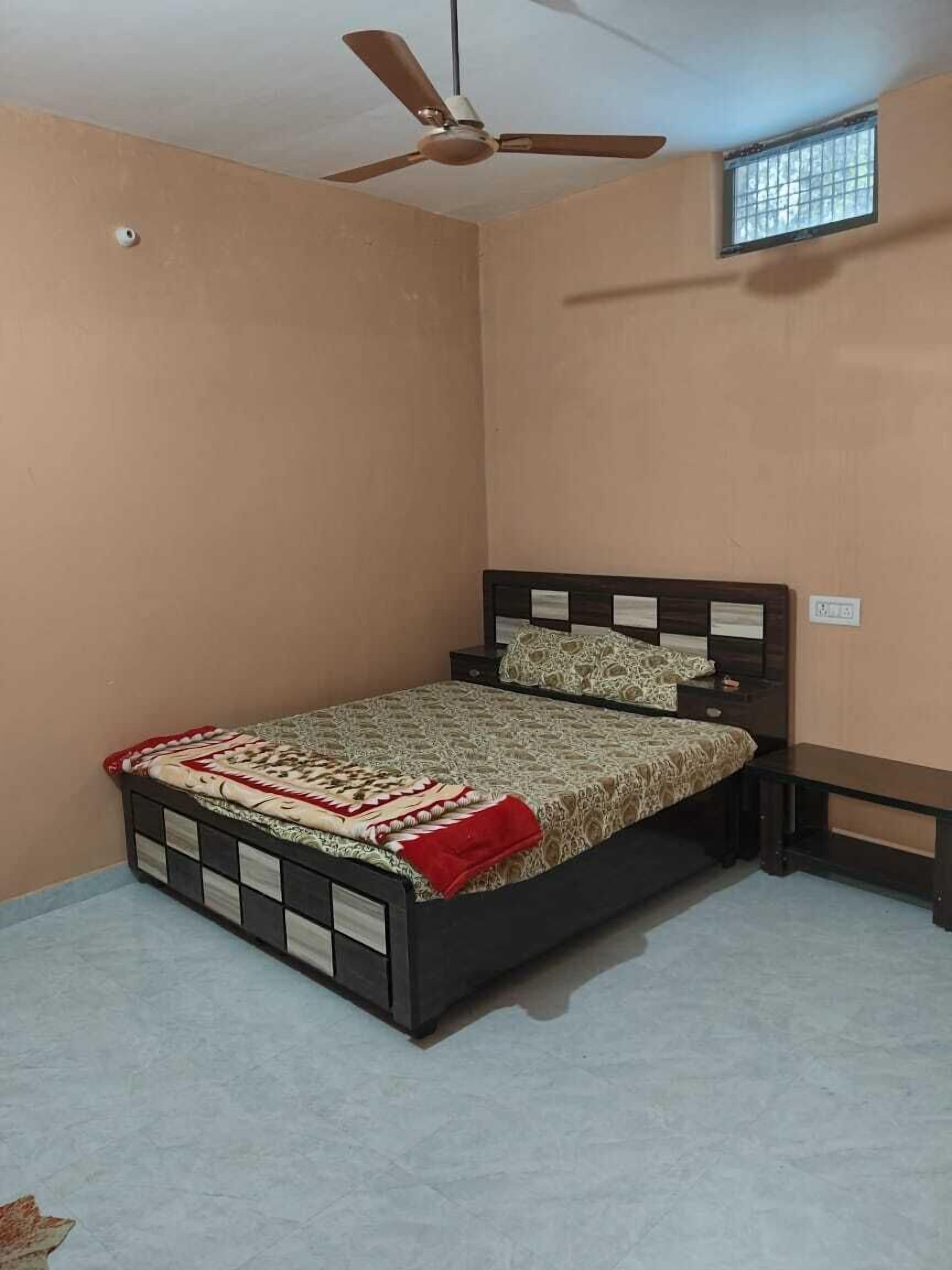 A bedroom with a bed, a ceiling fan, a window, and a wall socket.