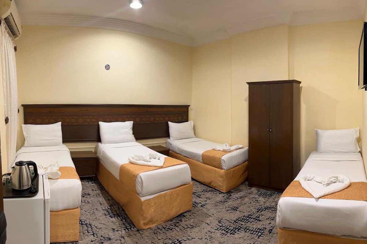 Ein Hotelzimmer mit drei Einzelbetten, einem Kleiderschrank, einem Fernseher und einem Wasserkocher auf dem Nachttisch.