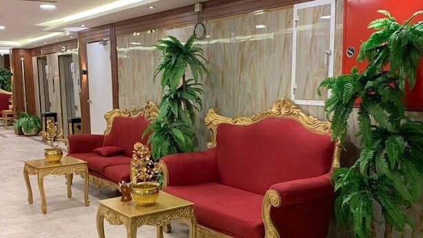 Et hotellobby med en rød sofa, møbler med gulddetaljer og potteplanter.