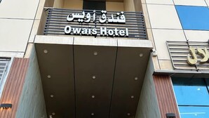 Indgangen til Owais Hotel med et moderne design, med et markant skilt på både arabisk og engelsk, en glasfacade og en metal trappe, der fører op til indgangen.