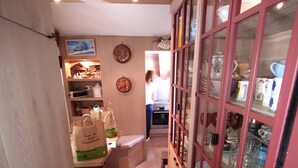 Ein schmaler Korridor mit Holzboden, einem Schrank mit Glastüren auf der rechten Seite und einer Küche im Hintergrund.