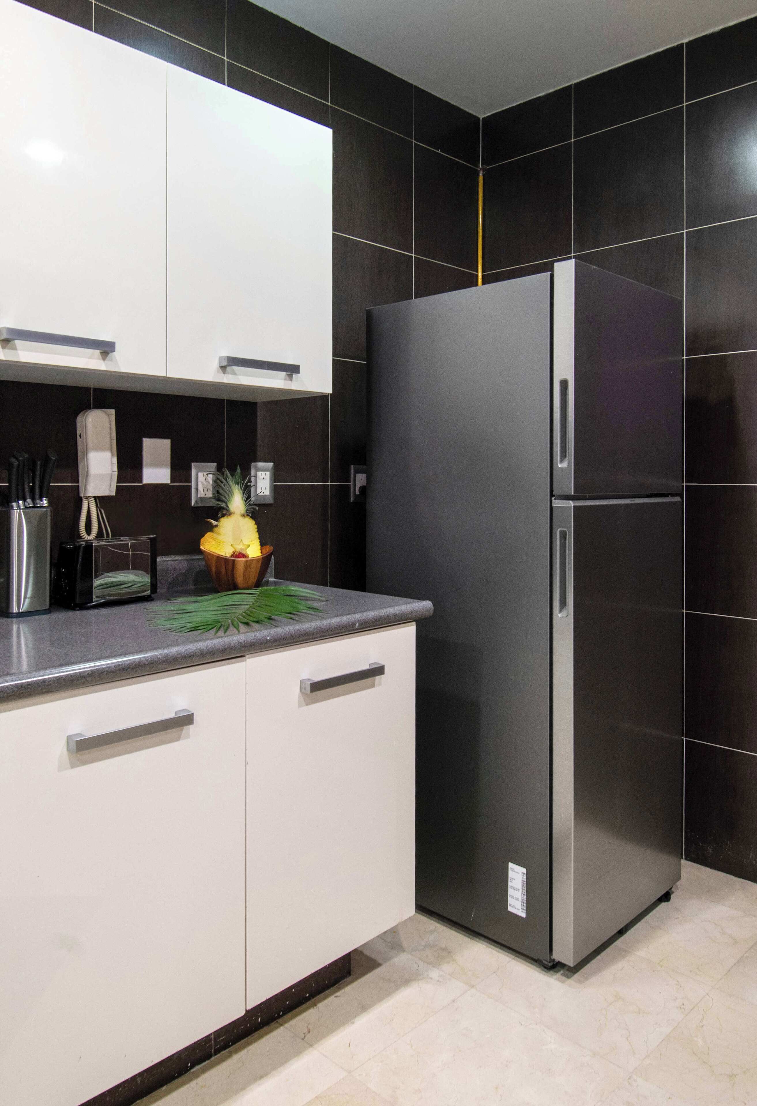Une cuisine moderne dotée d’un réfrigérateur en acier inoxydable, de meubles blancs et d’un dosseret de crédence en carreaux noirs.