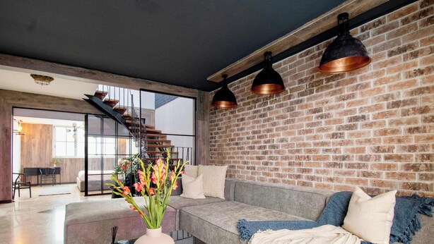 A modern living room with a glass coffee table, a sofa with a throw blanket, and a brick wall. - La Chula · Stylish Home in Condesa + Rooftop Bar (Mexico City)