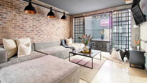A modern living room with a brick wall, grey sofas, a glass coffee table, and pendant lighting. - La Chula · Stylish Home in Condesa + Rooftop Bar (Mexico City)