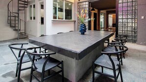 A modern interior with a large central island table surrounded by chairs, a spiral staircase, and string lights. - La Chula · Stylish Home in Condesa + Rooftop Bar (Mexico City)