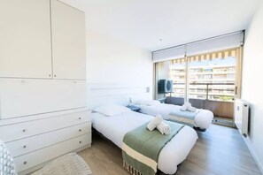 Ein modernes Hotelzimmer mit zwei Betten, einem großen Kleiderschrank und Blick auf die Stadt durch große Fenster.