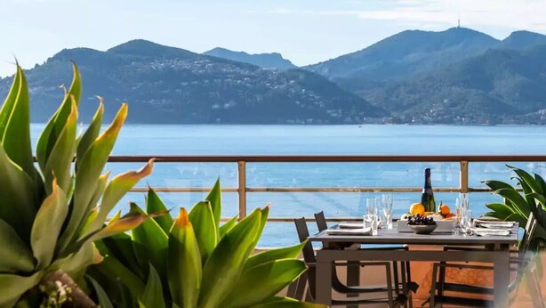 Une table dressée pour le dîner, avec une vue sur la mer et les montagnes en arrière-plan.