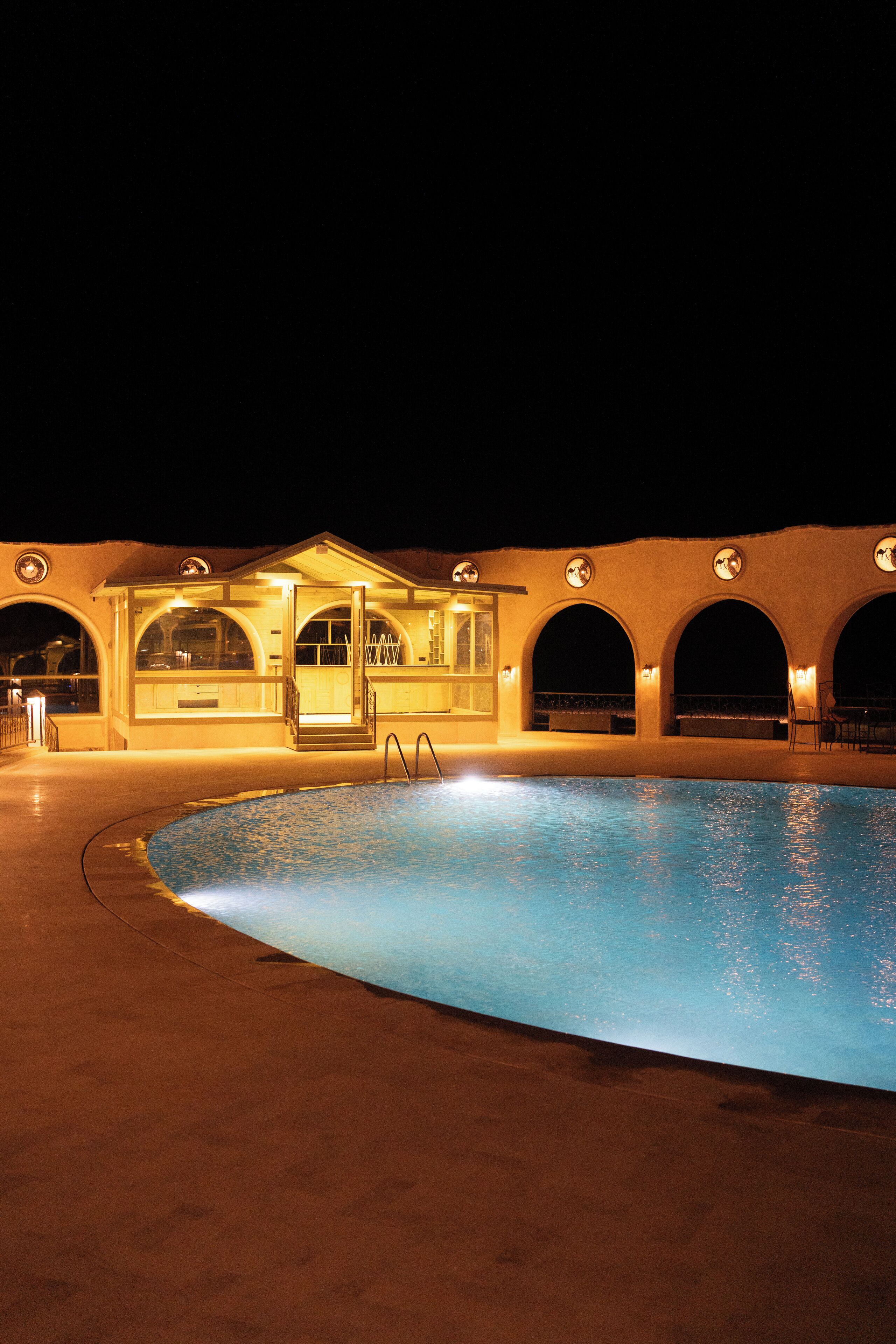 A swimming pool with a covered area featuring arched doorways and a small building with a door open.