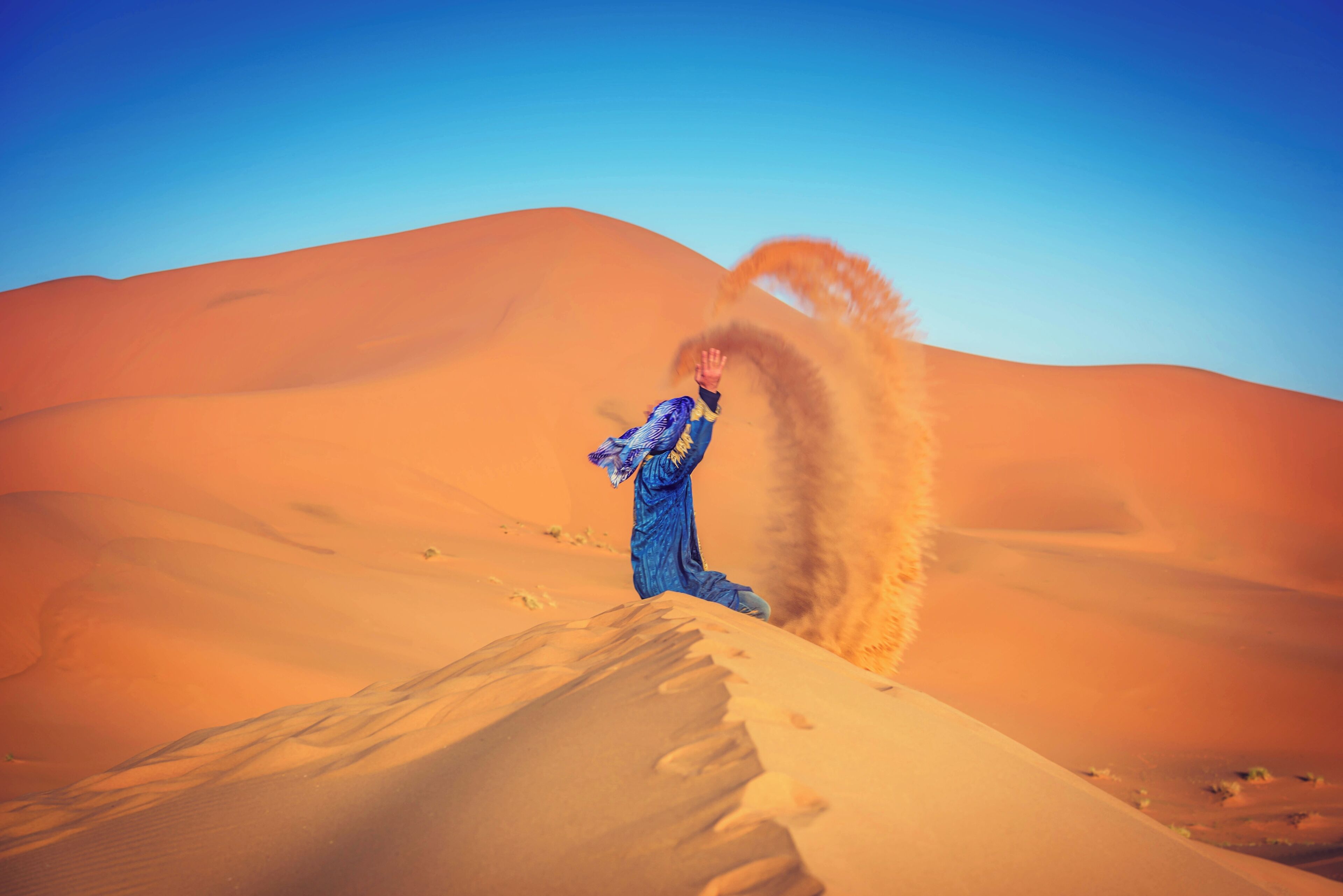 A person in a blue outfit in a desert landscape with sand dunes.