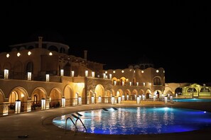 A pool area with a curved pool and a building with arched windows and balconies. - Nasser Palace Suites & Spa (Taouz)