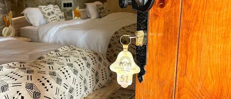 Una puerta de madera con un ojo de cerradura y una llave, una cama con ropa de cama estampada, una pared de piedra y una lámpara colgante.