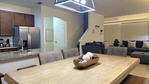 A modern kitchen with a built-in refrigerator, a dining area with a wooden table and chairs, and a staircase leading to a living area with a sofa and a coffee table. - Family Home 20 min Disney - 4BR - Heated Pool - BBQ (Kissimmee)