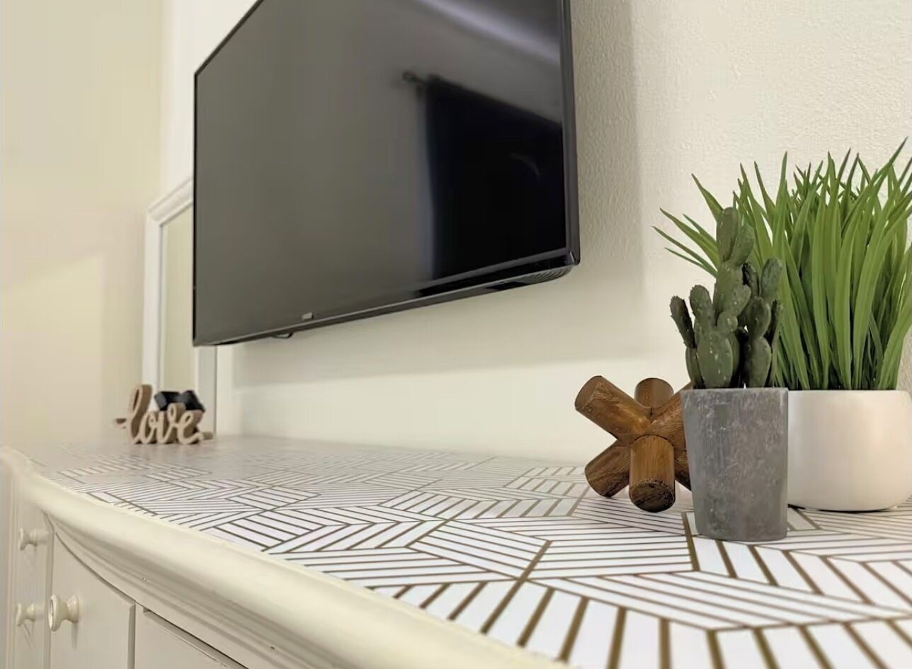 Een moderne keuken met een aanrecht met een geometrisch patroon, een flatscreen televisie erboven, een cactusplant en een houten sculptuur.