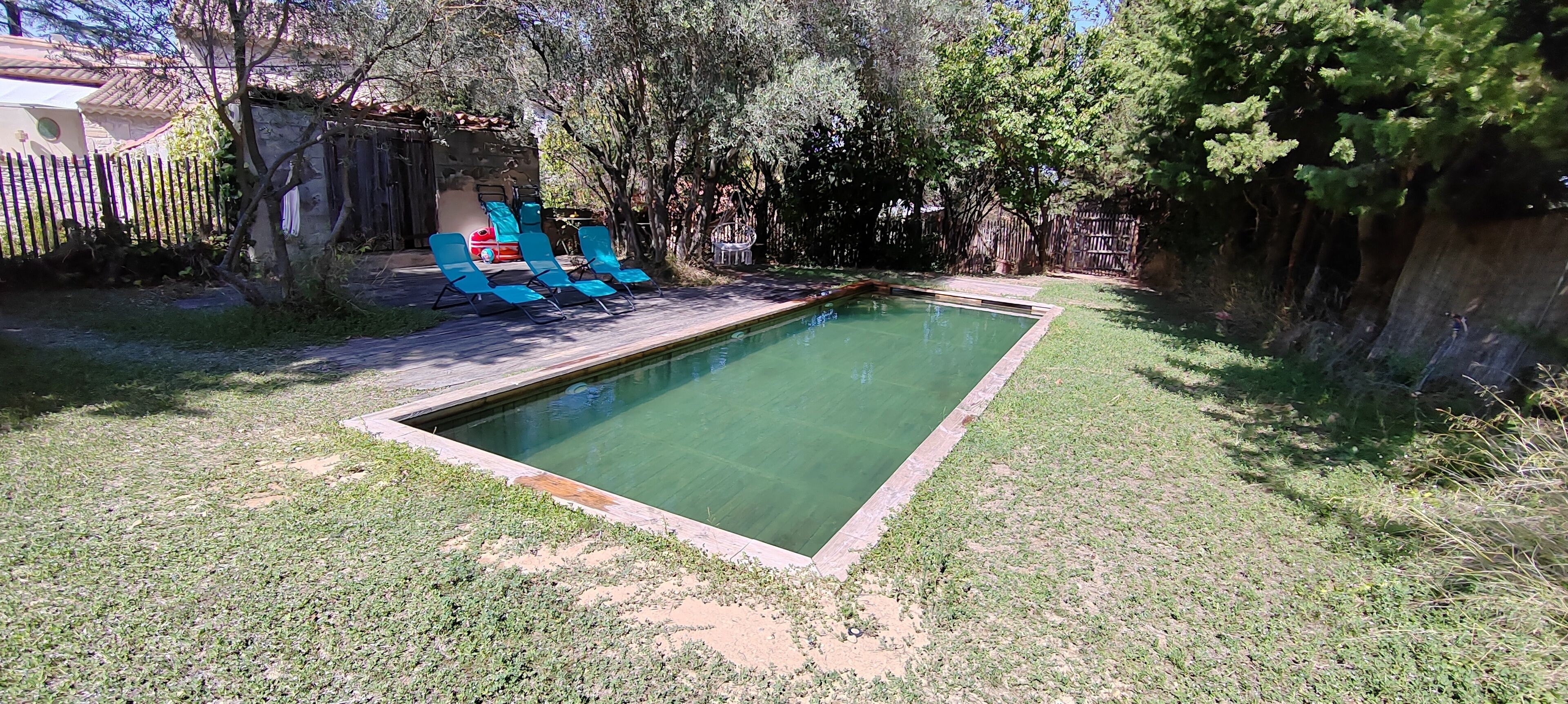 En rektangulär swimmingpool med ett trädäck och blå solstolar.