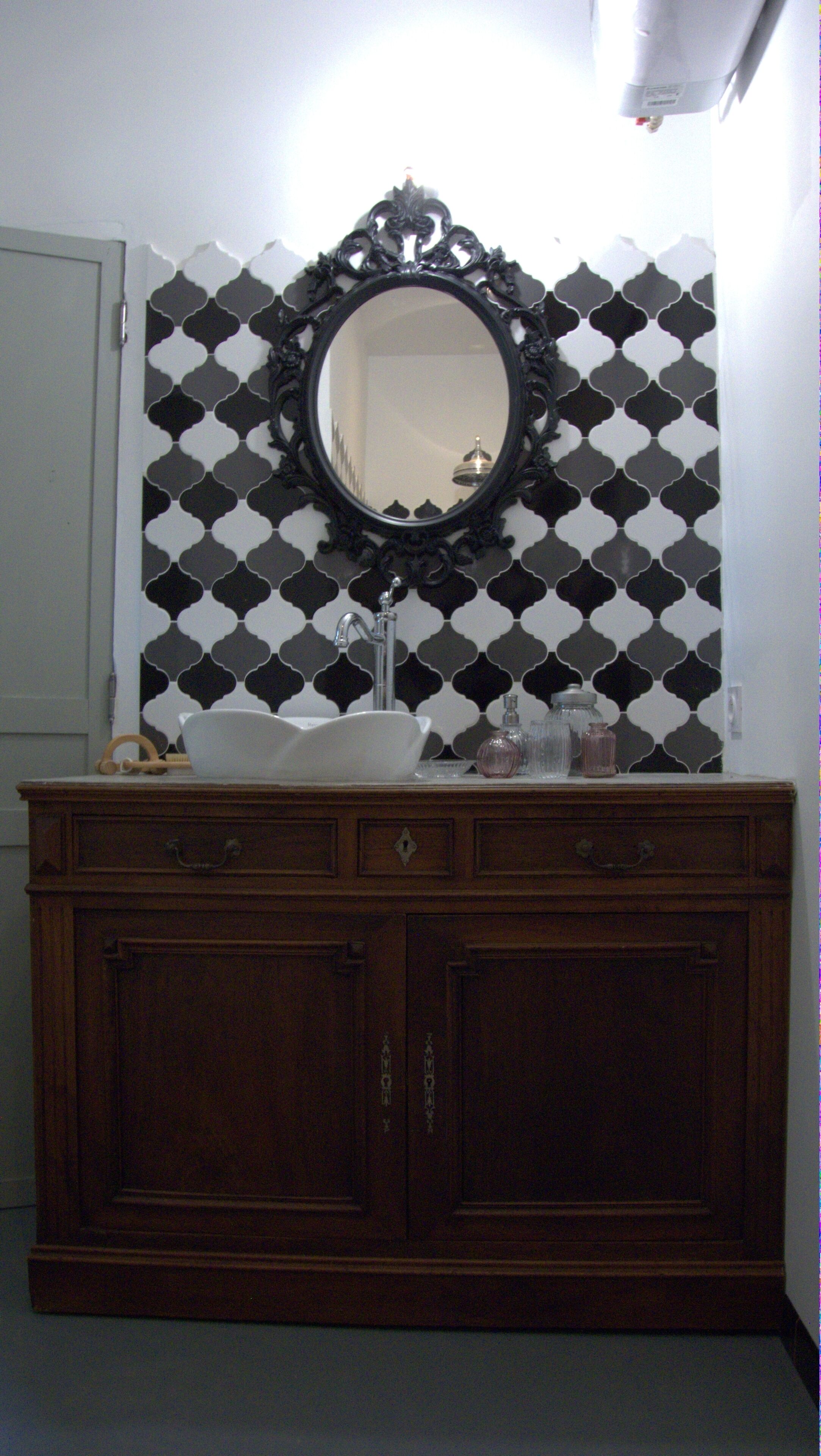 A bathroom with a black and white patterned wall, a round mirror, a white sink, and a wooden vanity with drawers.