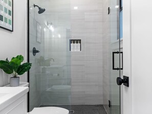 A modern bathroom with a glass shower enclosure, a white sink, a potted plant, and a tiled floor. - 5BR3B By Subway Downtown (Boston)