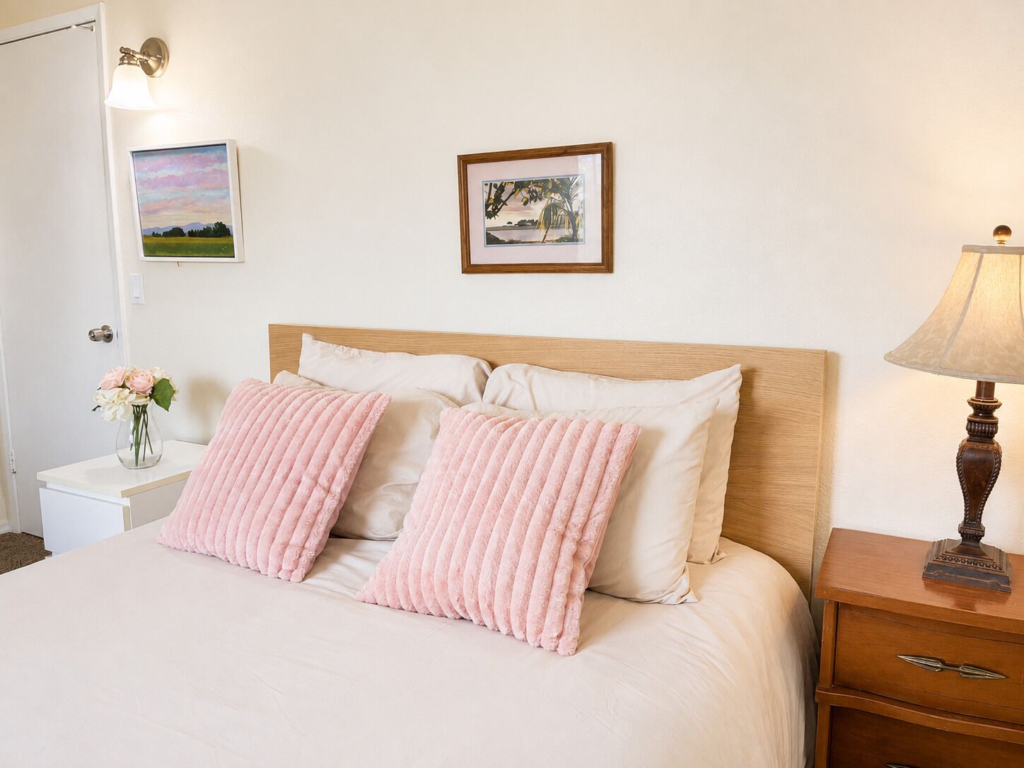 Un lit bien fait, orné de deux coussins roses, une table de chevet avec un vase de fleurs et une lampe sur la table de nuit.