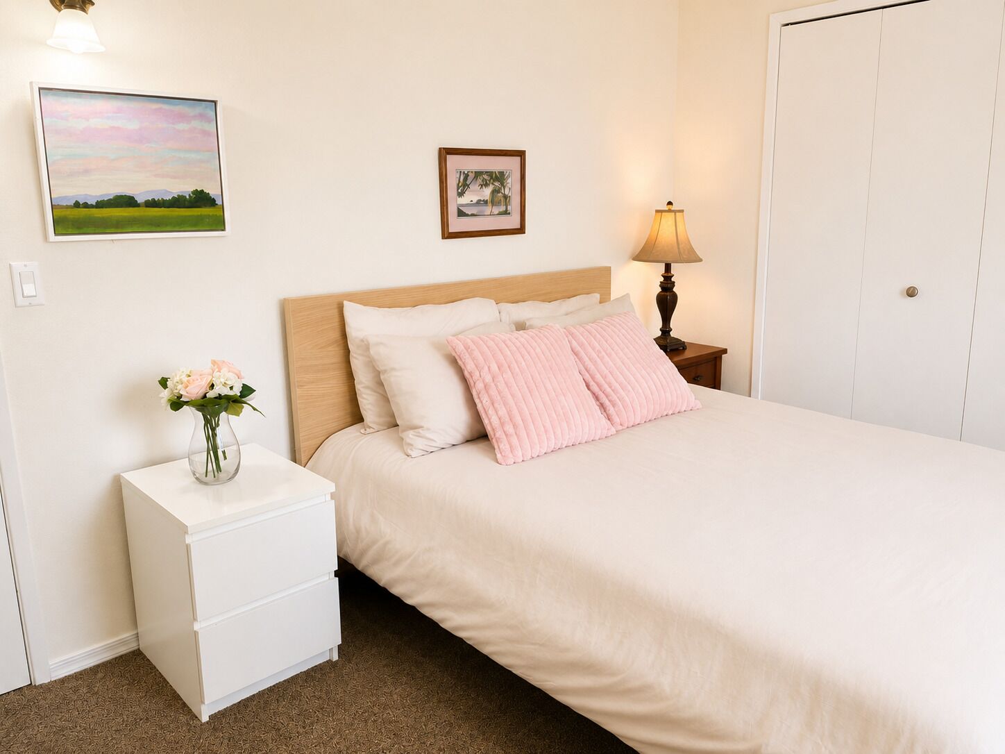 A bedroom with a bed, bedside table, lamp, and two framed pictures on the wall.
