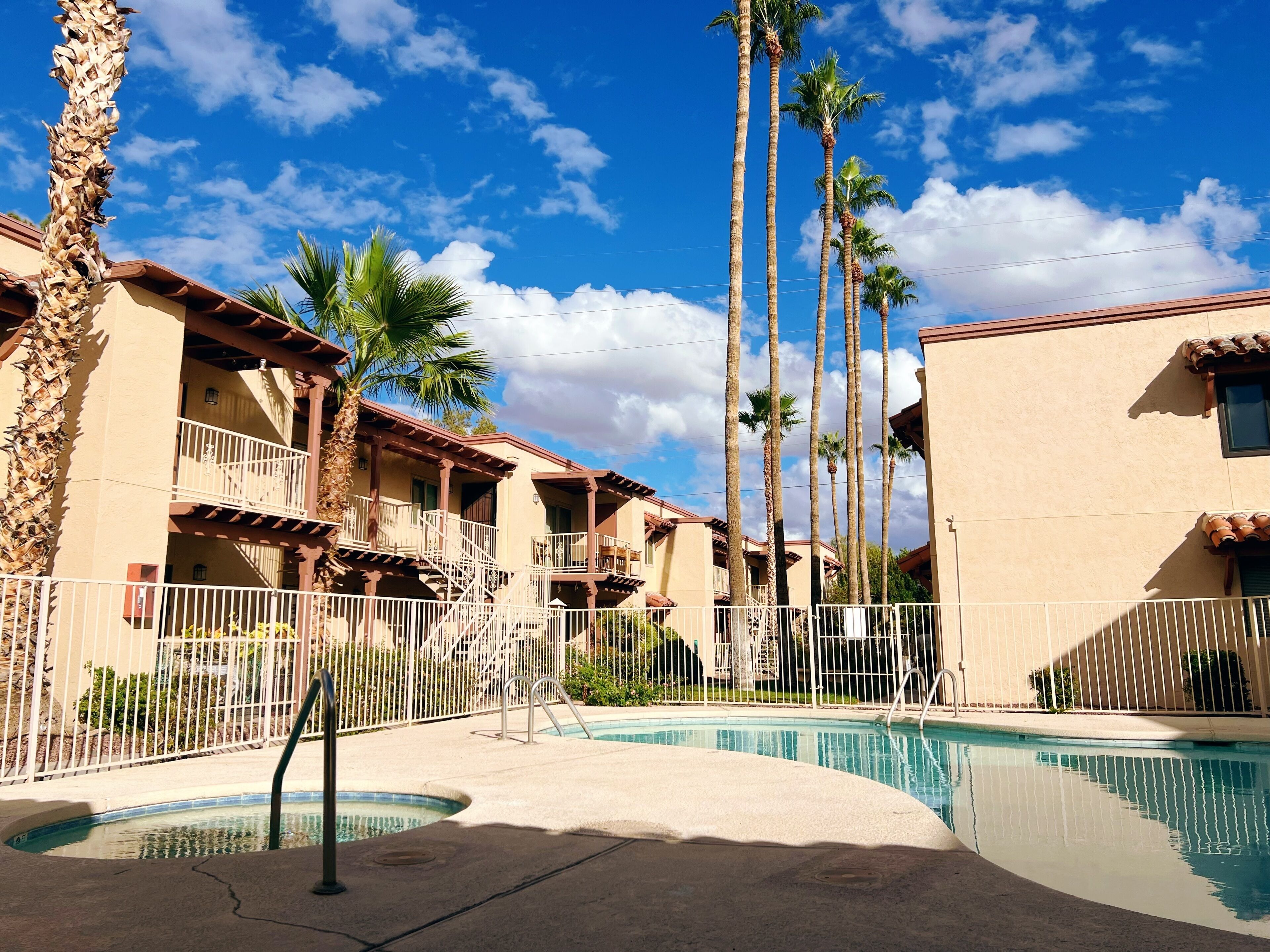 A pool area with a clear sky, palm trees, and a building with balconies.